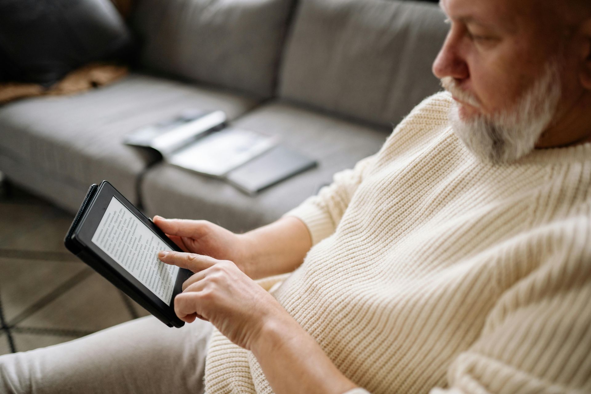 Man using a tablet on a couch, reading an e-book in a living room