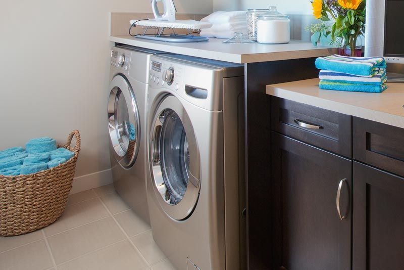 Laundry room with silver washer and dryer, dark cabinets, countertop items, and a blue towel basket
