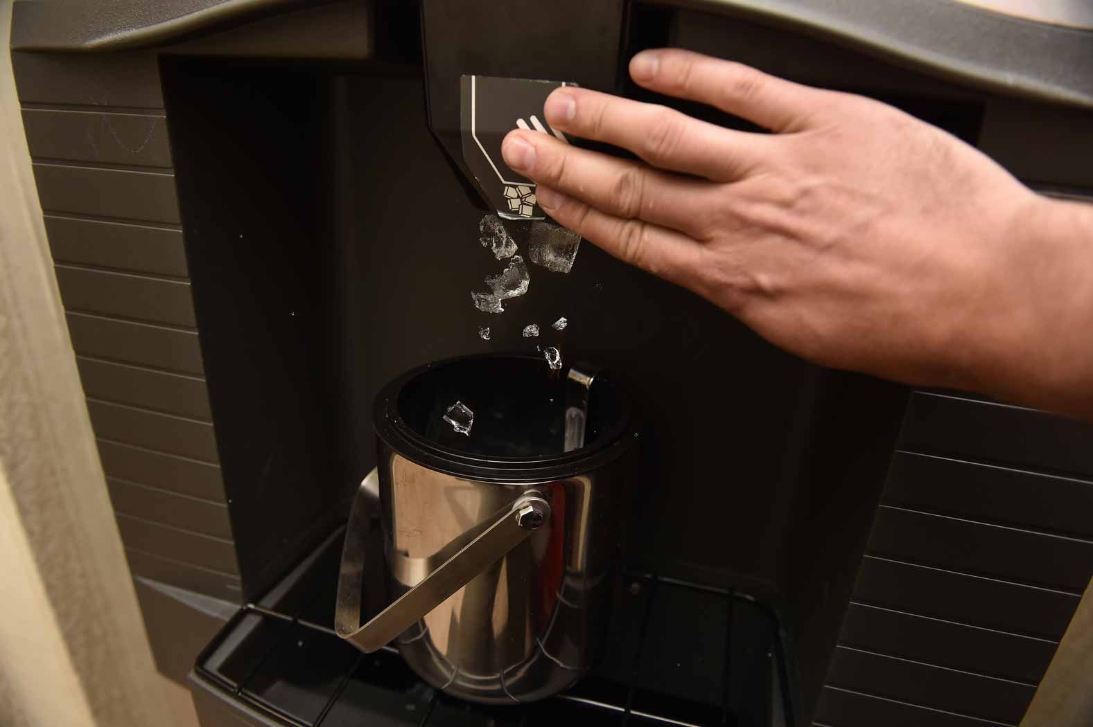 Hand pouring water into a metal coffee maker reservoir on a counter