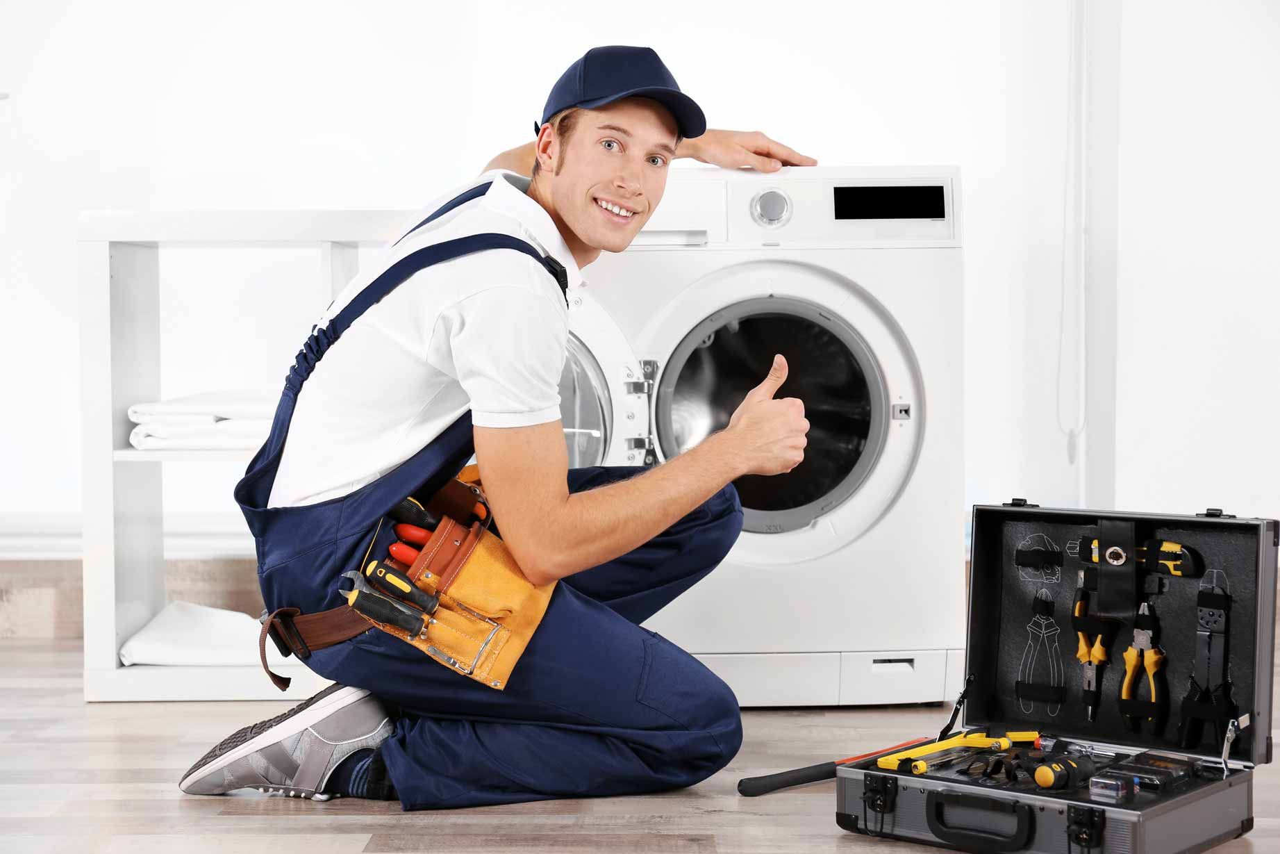 Appliance repair technician kneeling beside an open front-load washing machine with tools nearby