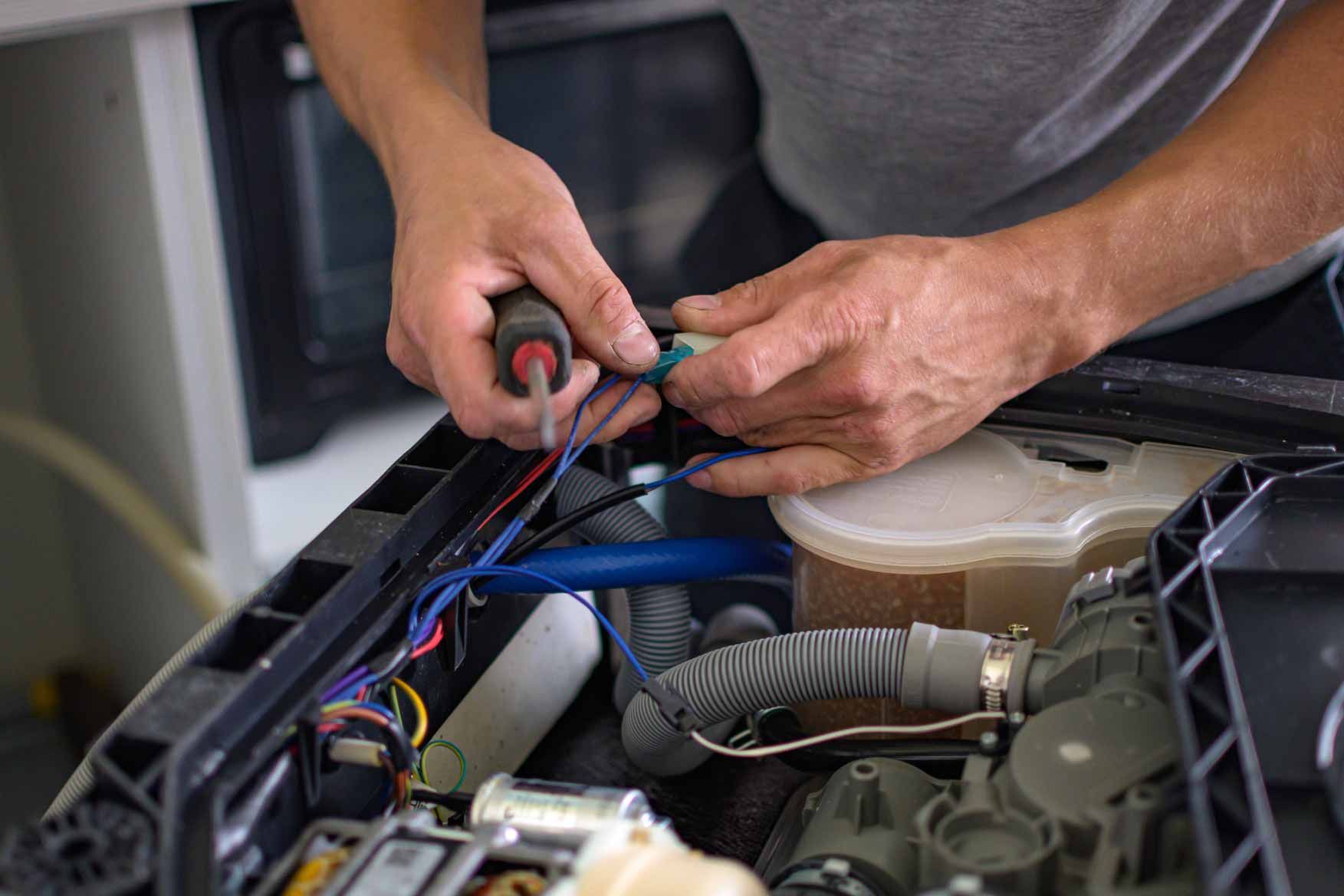 Hands wiring components inside an open appliance with visible cables and tools