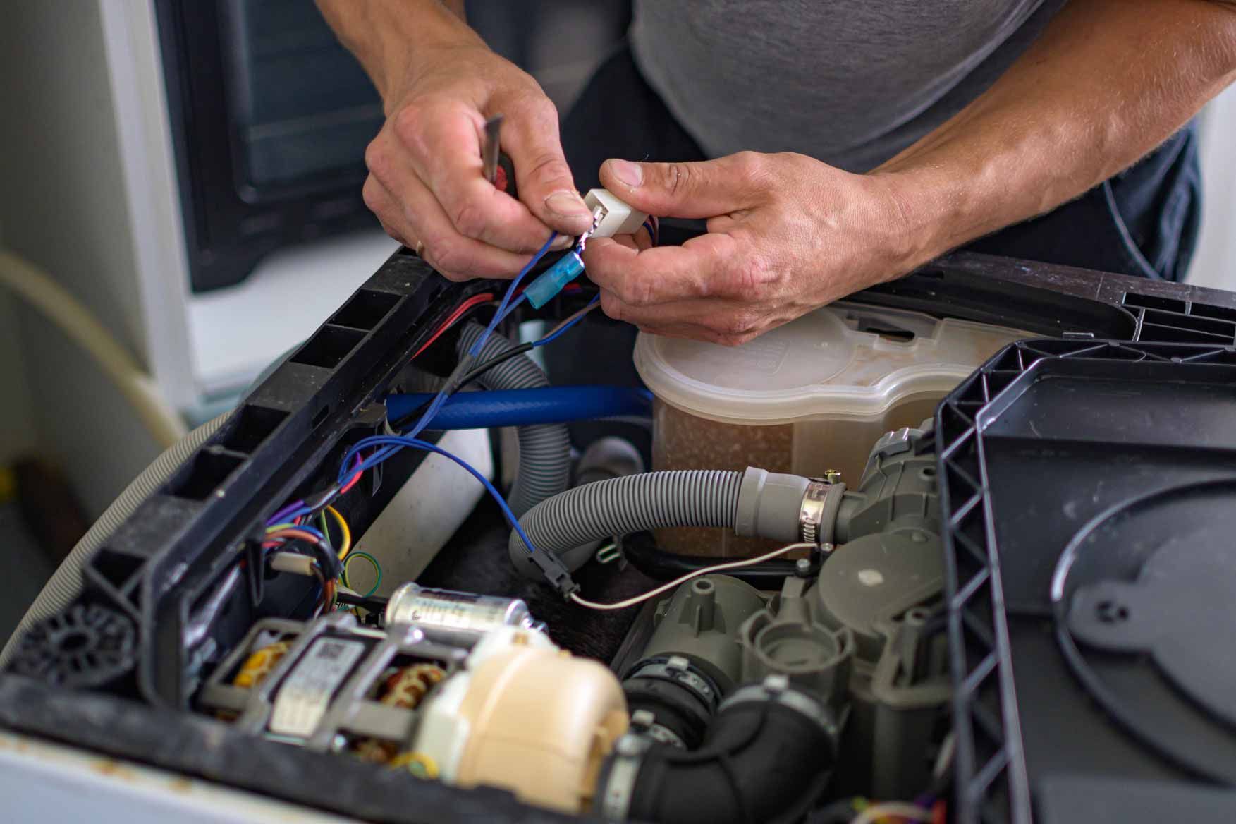 Hands repairing wiring inside an open appliance with visible motor and tubing