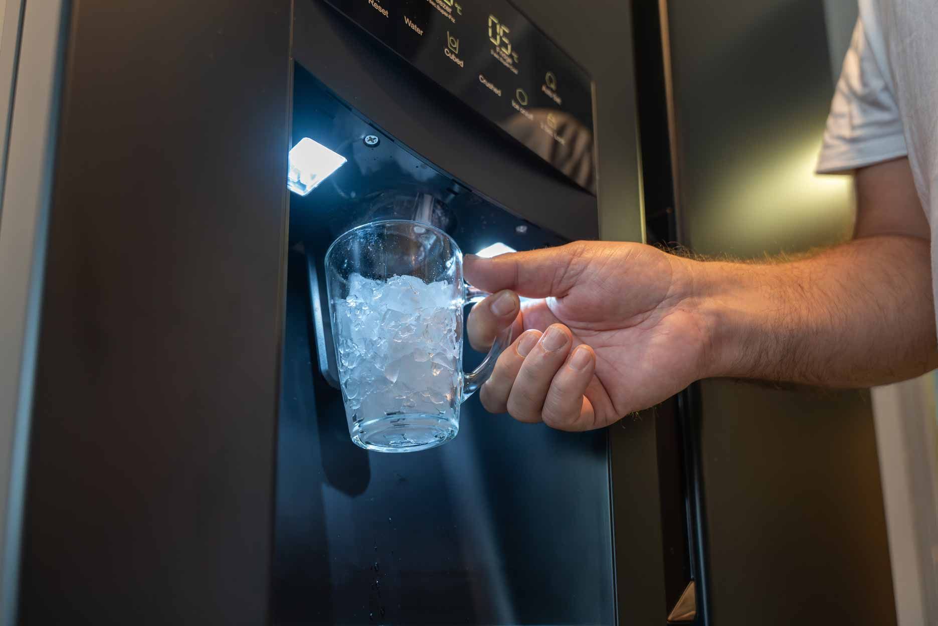 Hand reaching into a black ice dispenser to grab a cup of ice