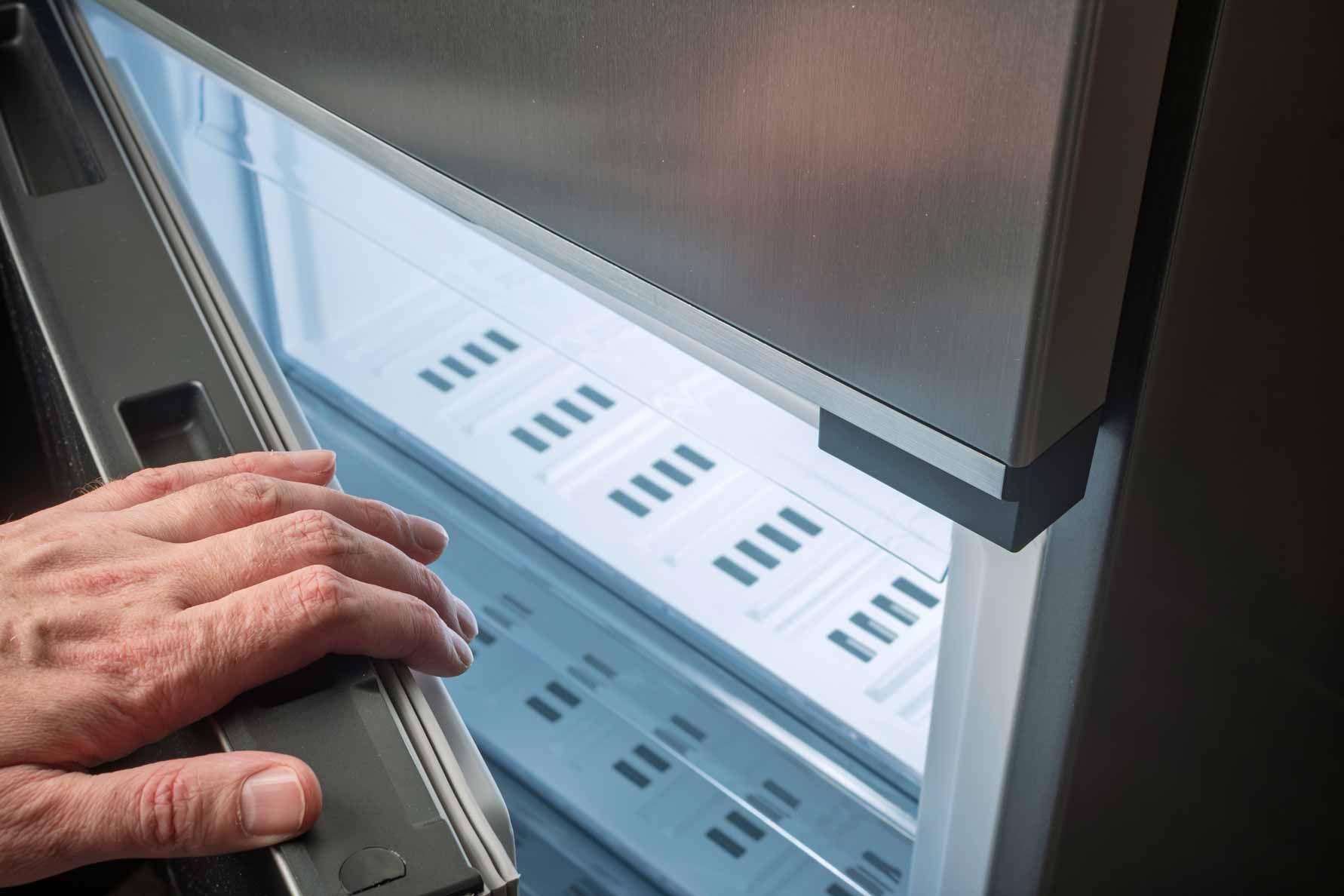 Hand opening a refrigerator door to reveal a white interior shelf inside a stainless steel appliance