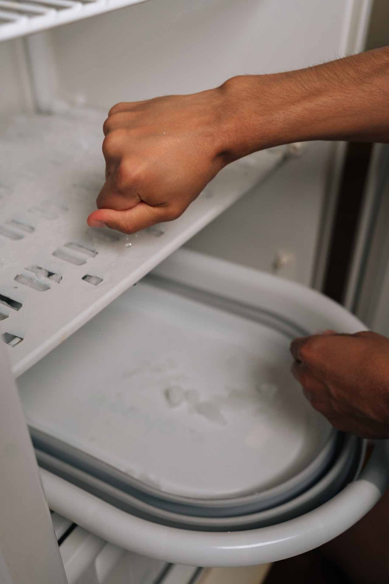 Hands opening a gray appliance door, with a white tray inside.