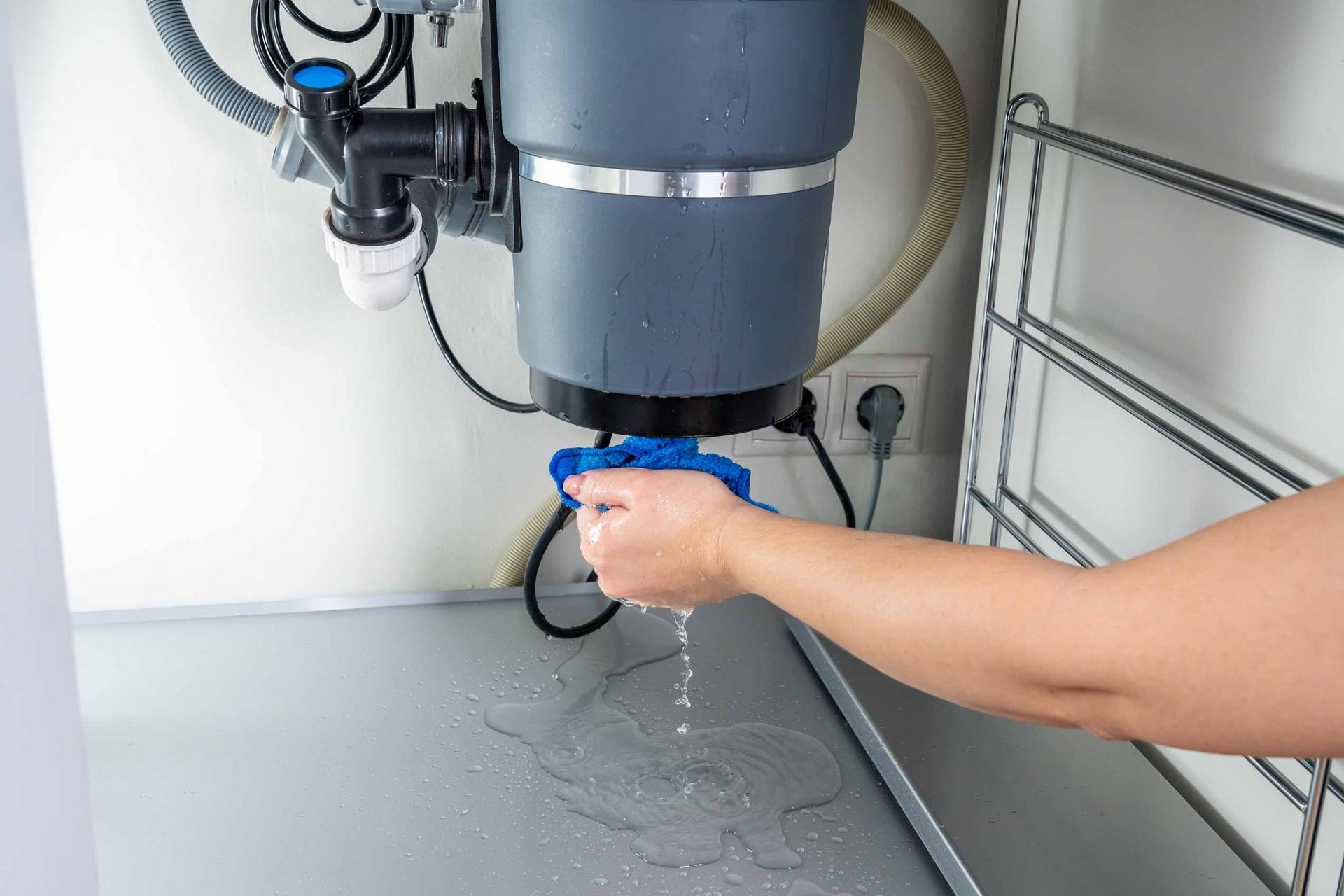 A person rinses a blue cup under a faucet beside a water heater in a utility room.