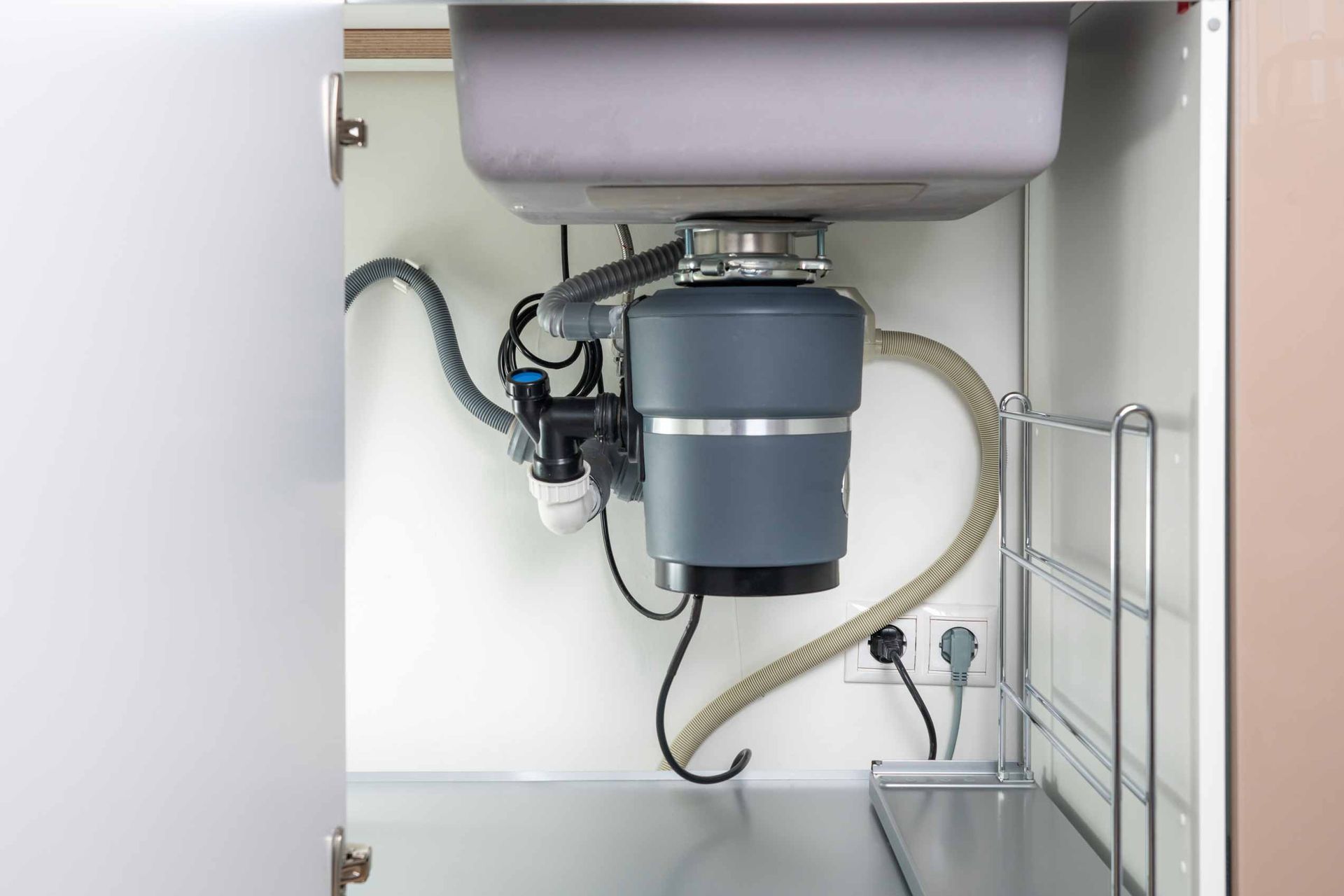 Under-sink garbage disposal and plumbing inside an open cabinet