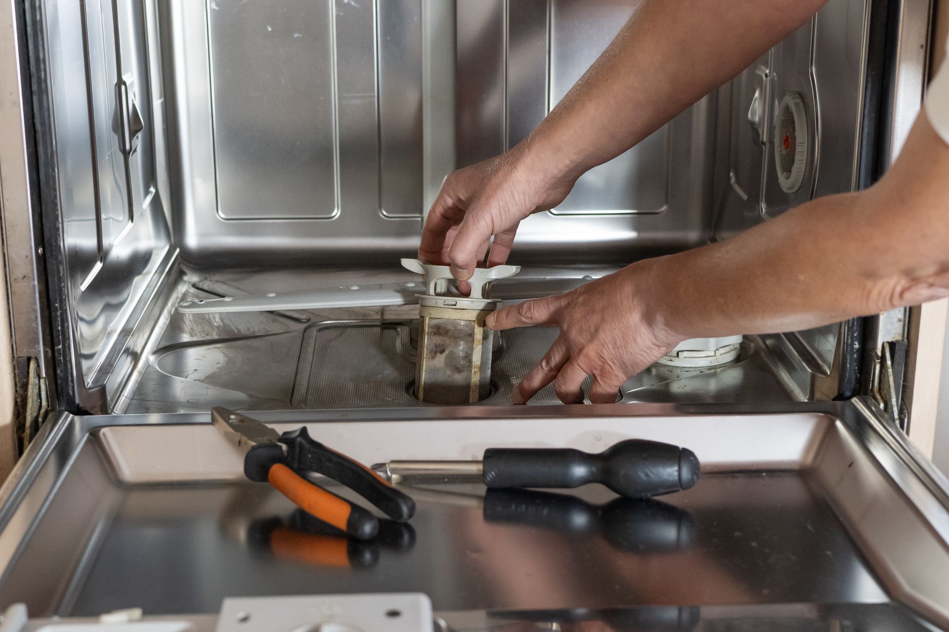 Hands adjusting a metal part inside a stainless steel appliance, with tools on the counter.