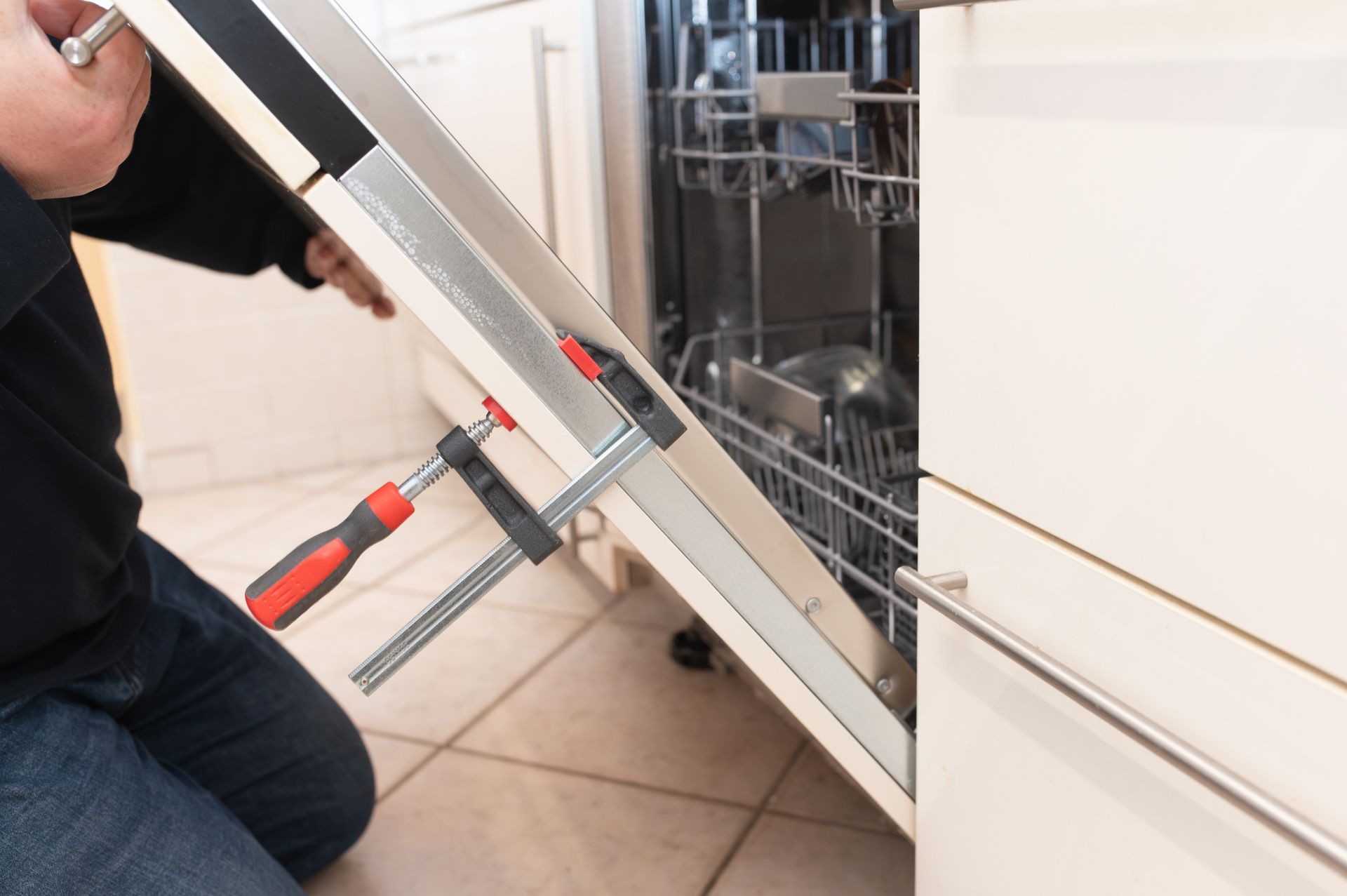 Person using a clamp to adjust a dishwasher door in a kitchen