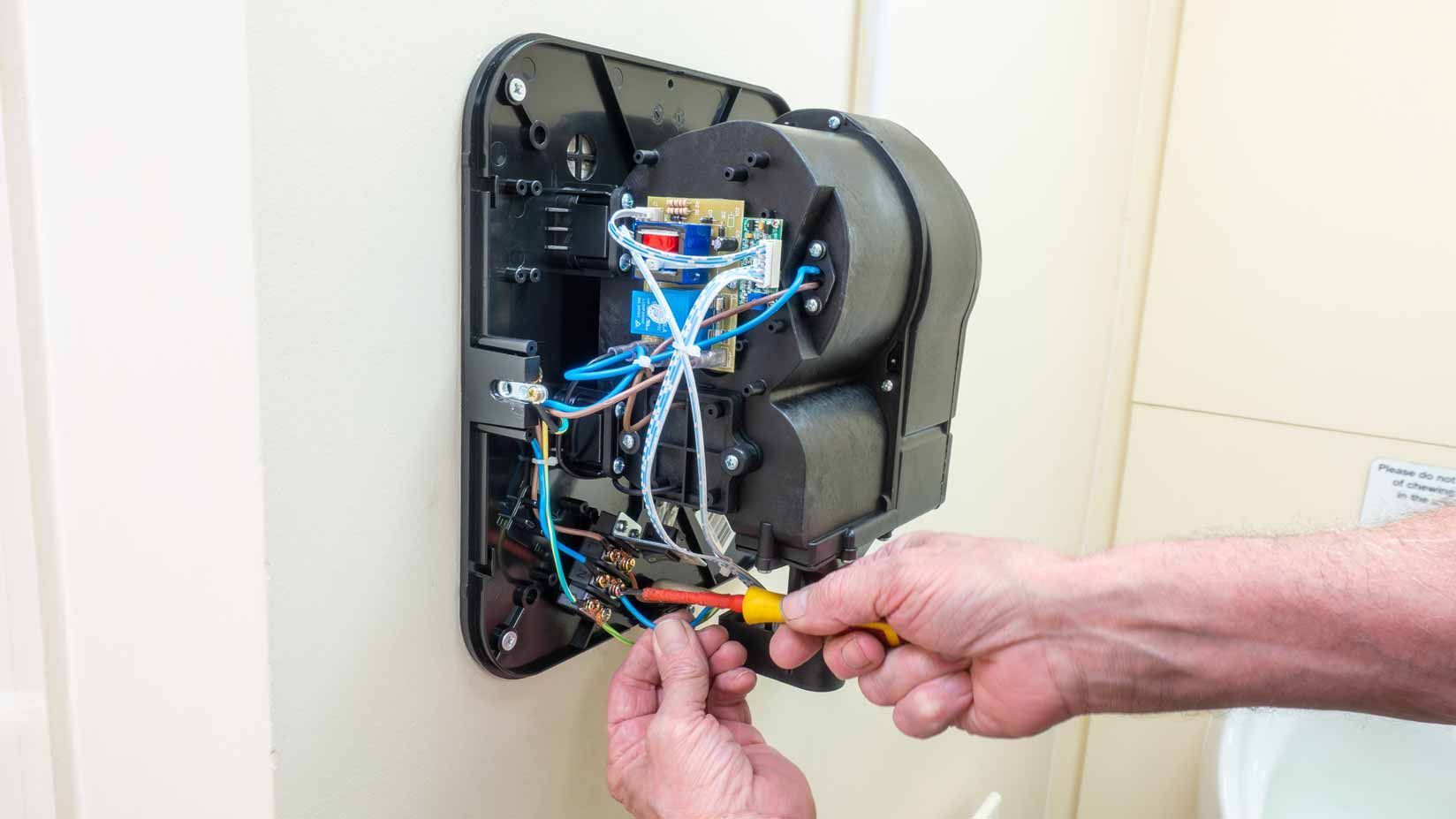 Hands wiring a wall-mounted electrical device with exposed blue and black cables.