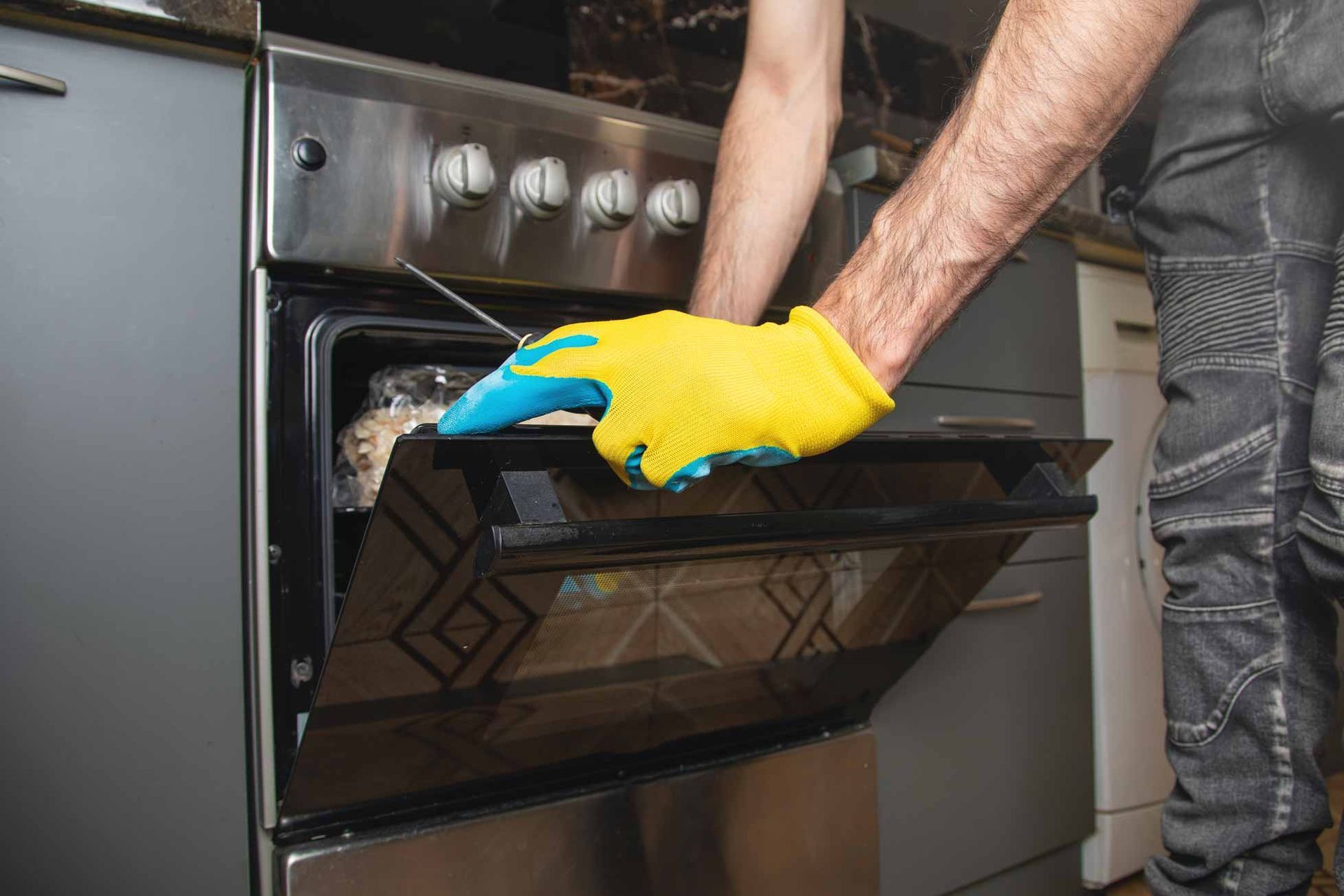 Person in yellow gloves cleaning an open oven door with a cloth in a kitchen