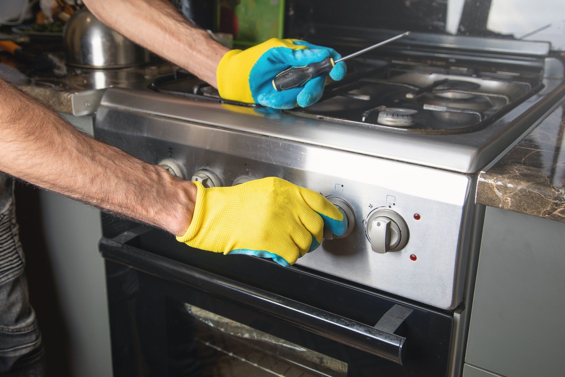 Yellow-gloved hands adjust a stove knob on a stainless steel oven.