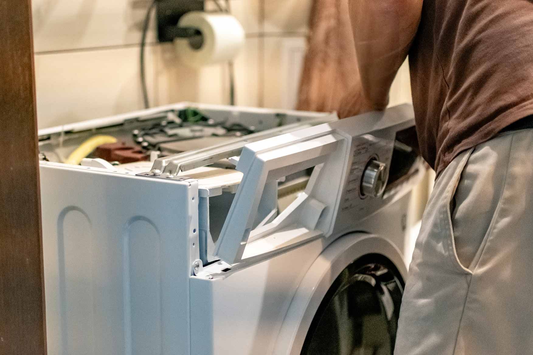 Person loading laundry into a white washing machine in a home laundry room
