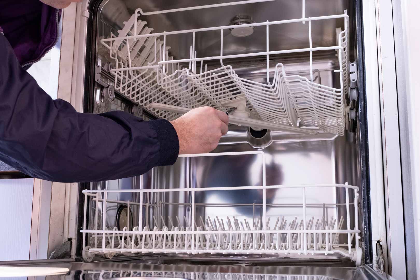 Person loading dishes into a stainless steel dishwasher with the door open