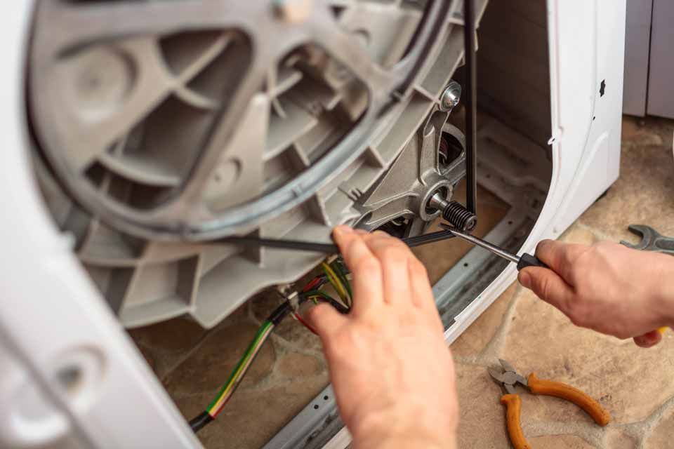 Technician repairing a dryer, handling wiring near the open back panel with tools nearby