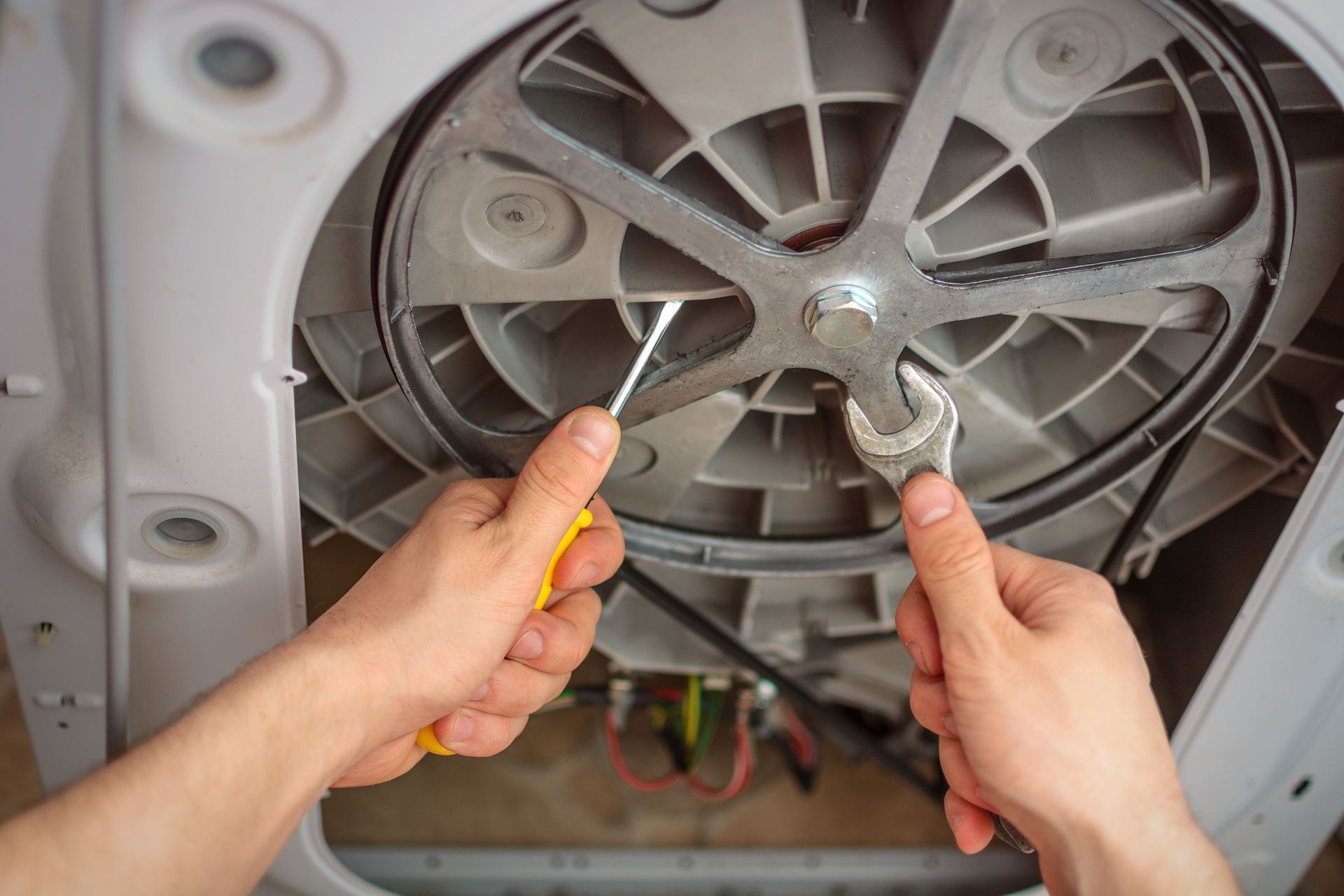 Hands using screwdrivers to repair a washing machine motor inside the opened back panel