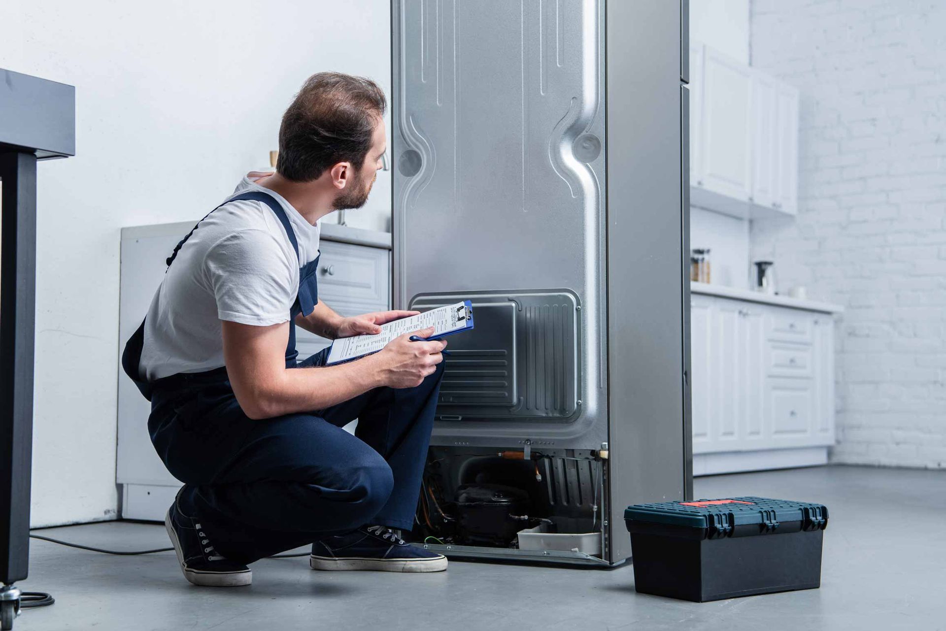 Technician kneeling beside open dishwasher, using tablet in a bright kitchen