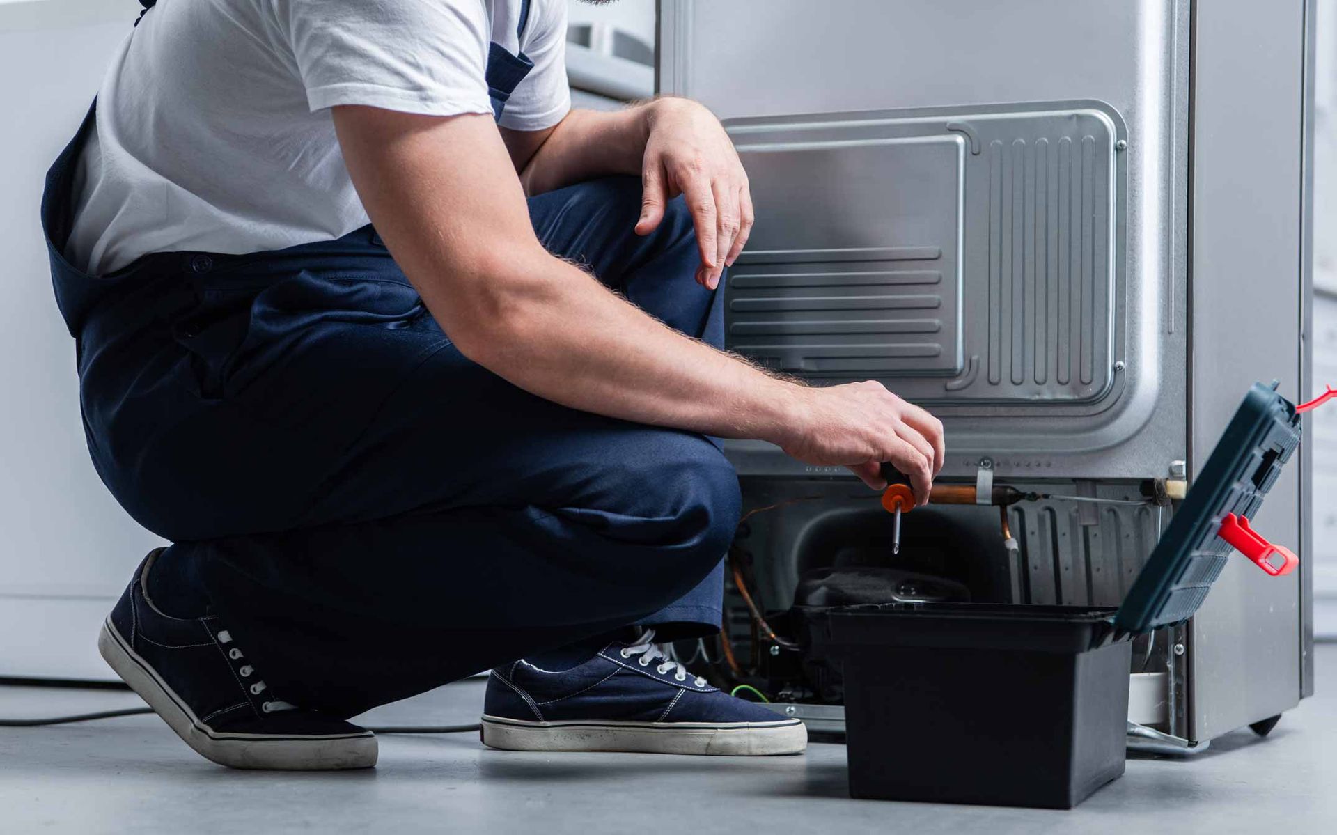 Technician kneeling by a wall-mounted HVAC unit, checking a leaking drain with a bucket and tools