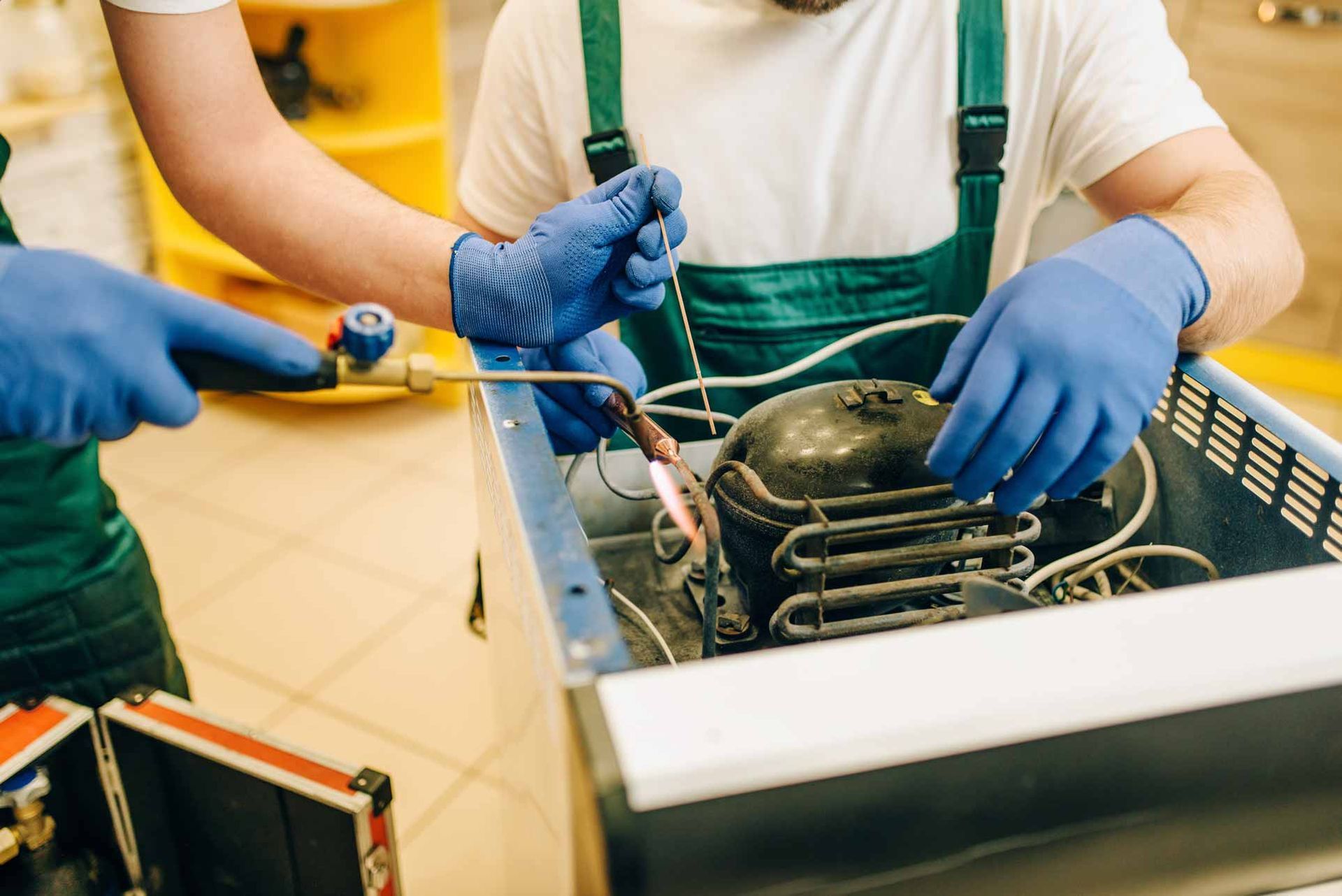 Technicians in blue gloves repairing a dishwasher with tools on a kitchen counter