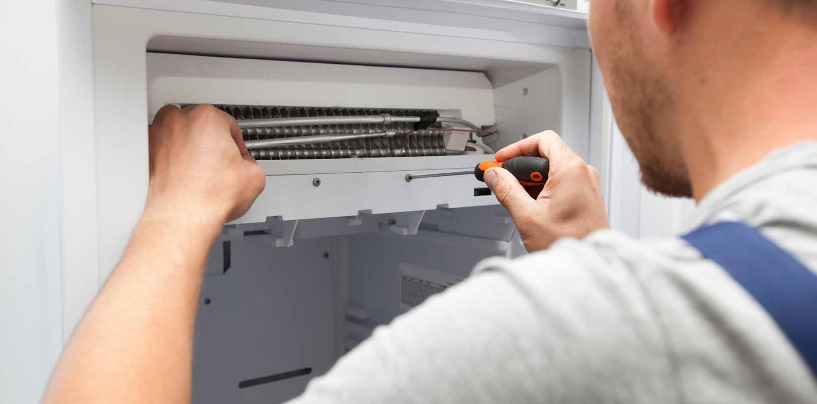 Technician using a screwdriver to repair an indoor air conditioner unit on a wall