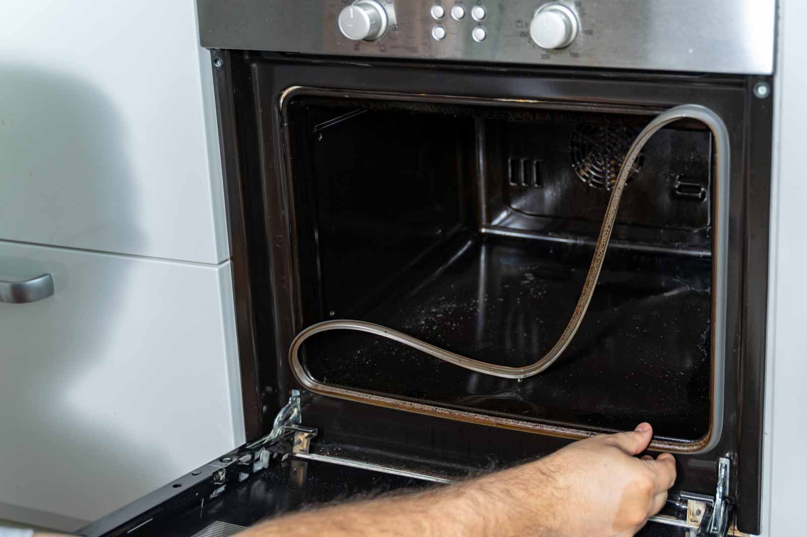 Person cleaning inside an oven with the door open and a coiled heating element visible.