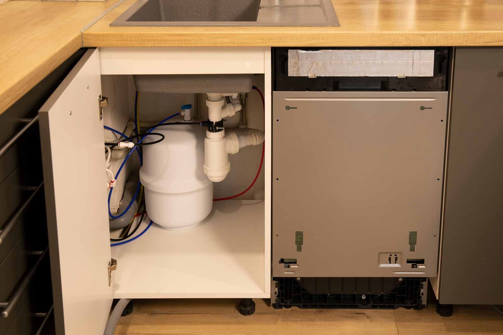 Under-sink cabinet with plumbing pipes and a dishwasher unit beside it