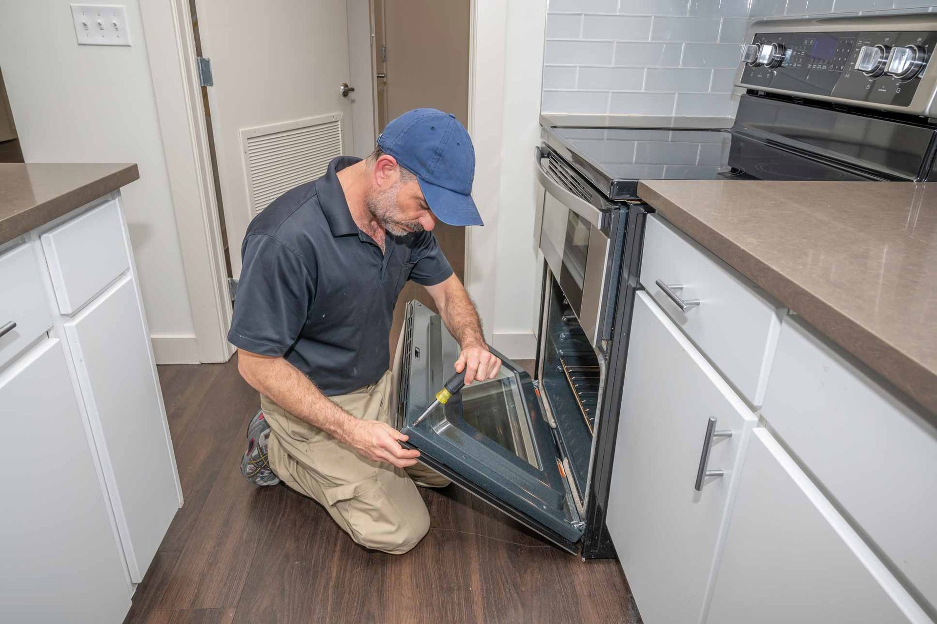 Technician kneeling to inspect a dishwasher in a modern kitchen