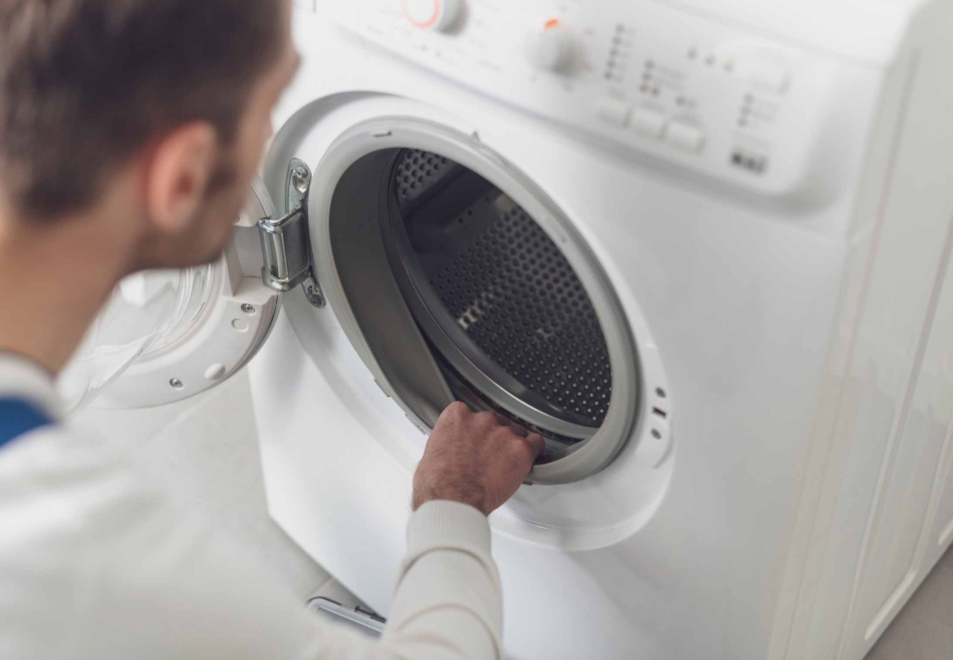Person loading a white front-load washing machine in a laundry room