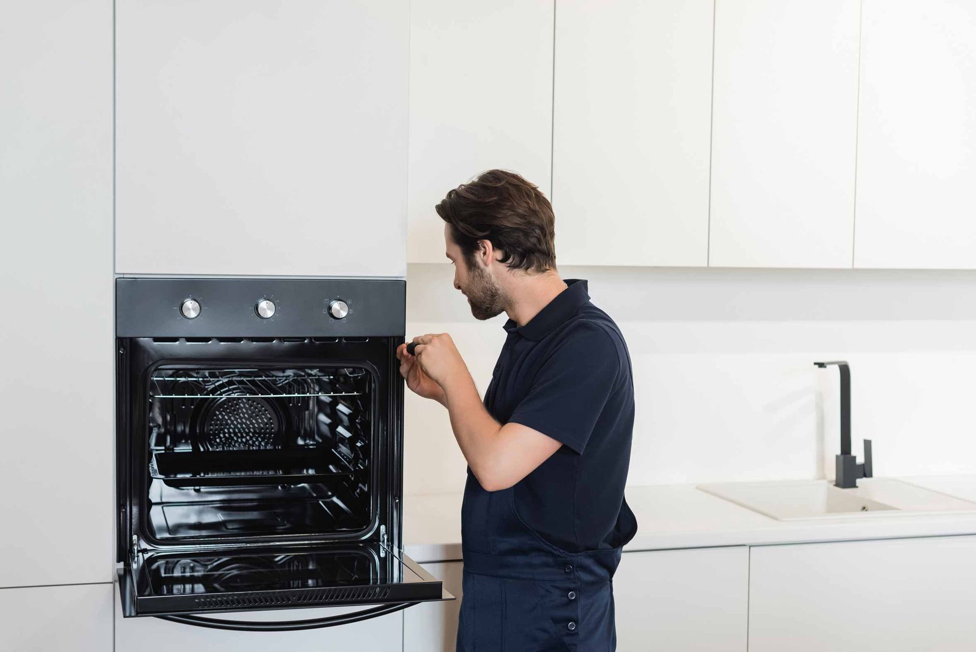 Man in a dark shirt inspecting an open black oven in a bright modern kitchen
