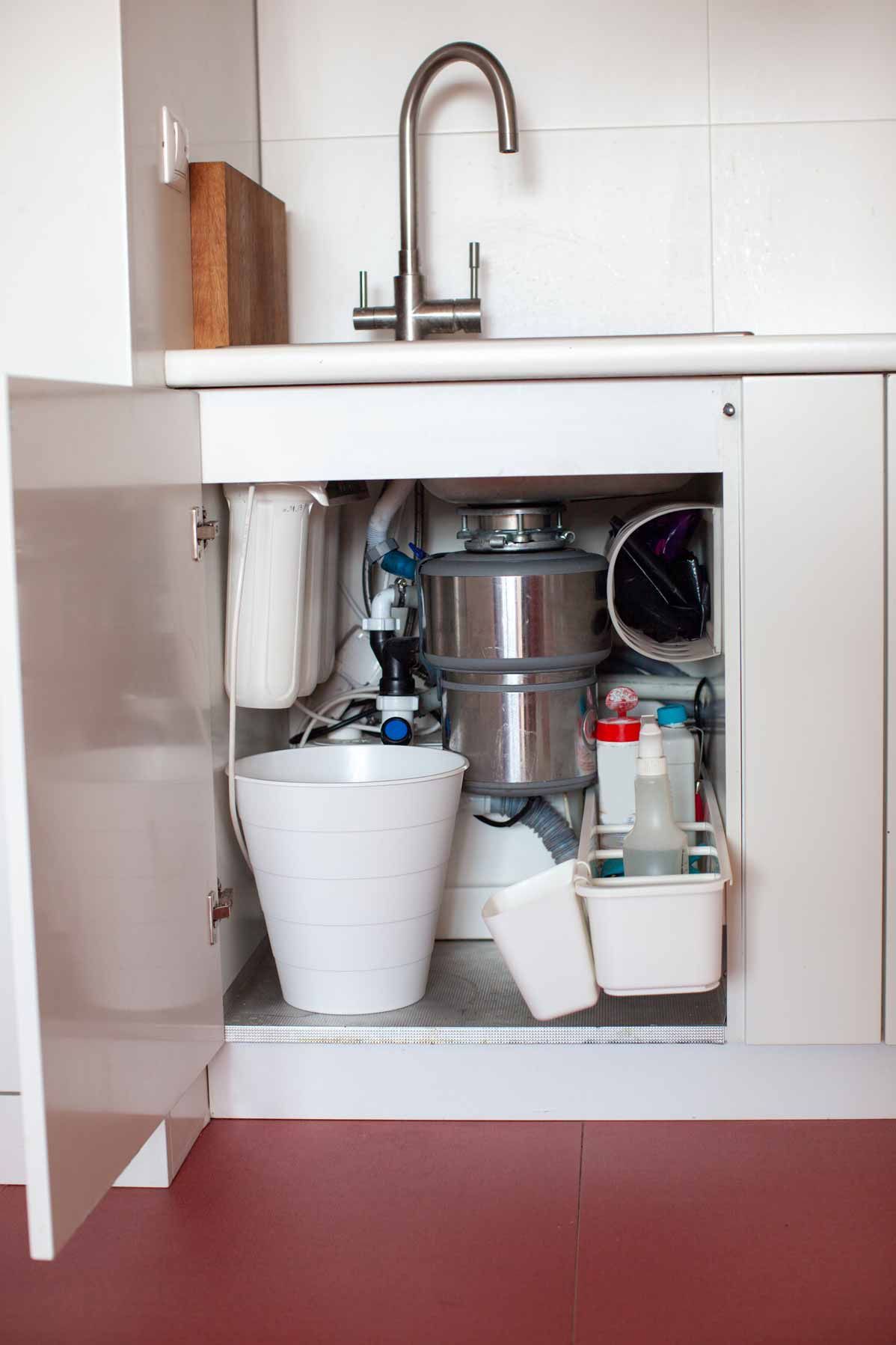 Open under-sink cabinet with cleaning supplies and buckets beneath a bathroom sink