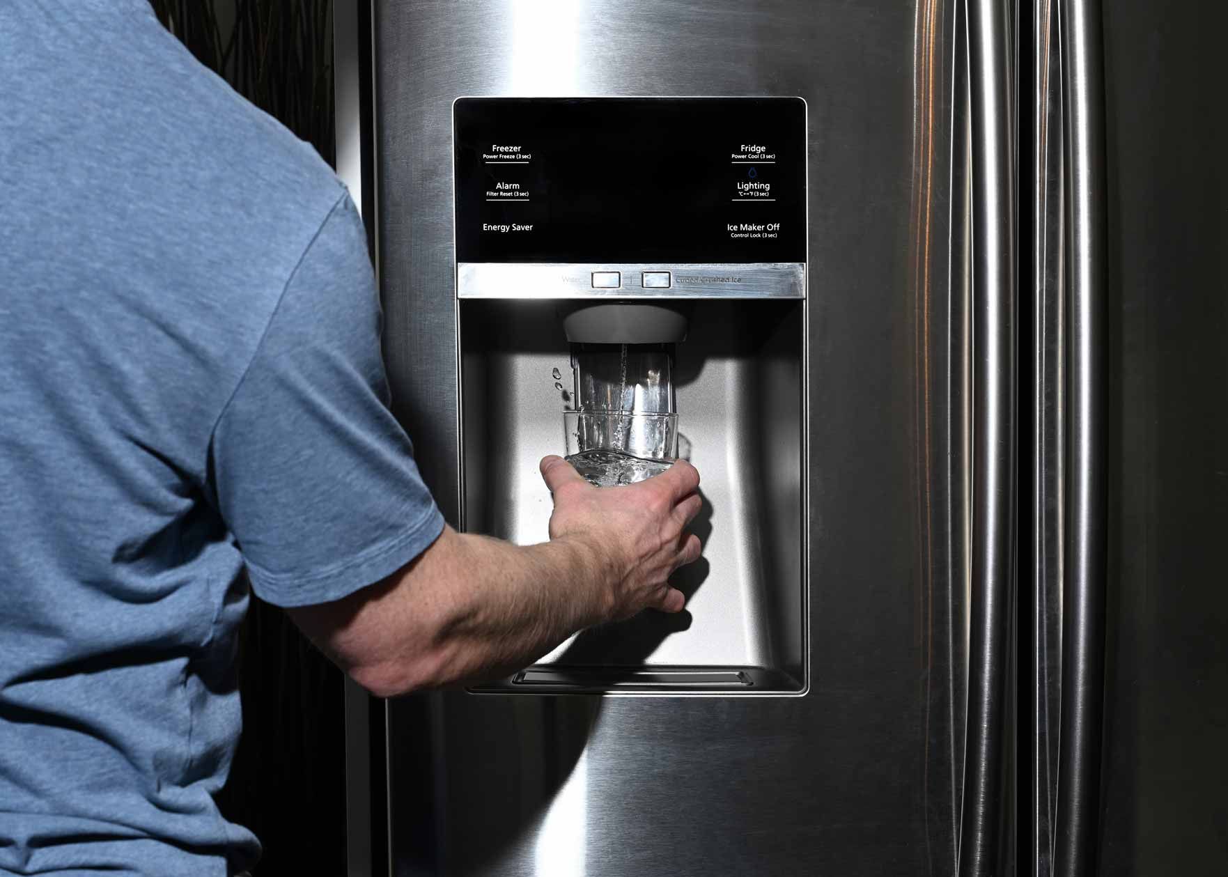 Person filling a glass at a stainless steel refrigerator water dispenser