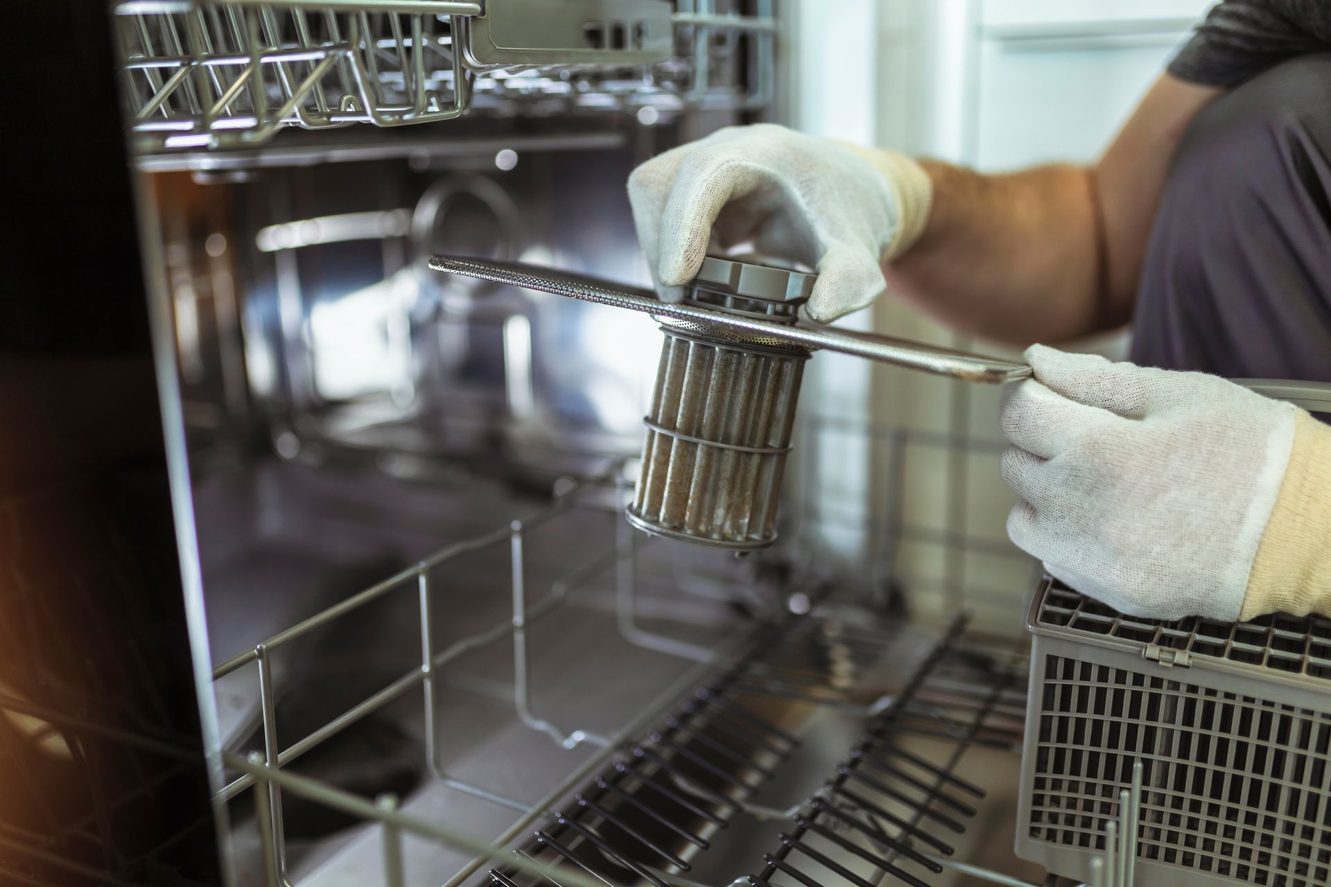 Gloved hands loading a metal utensil basket into a commercial dishwasher.