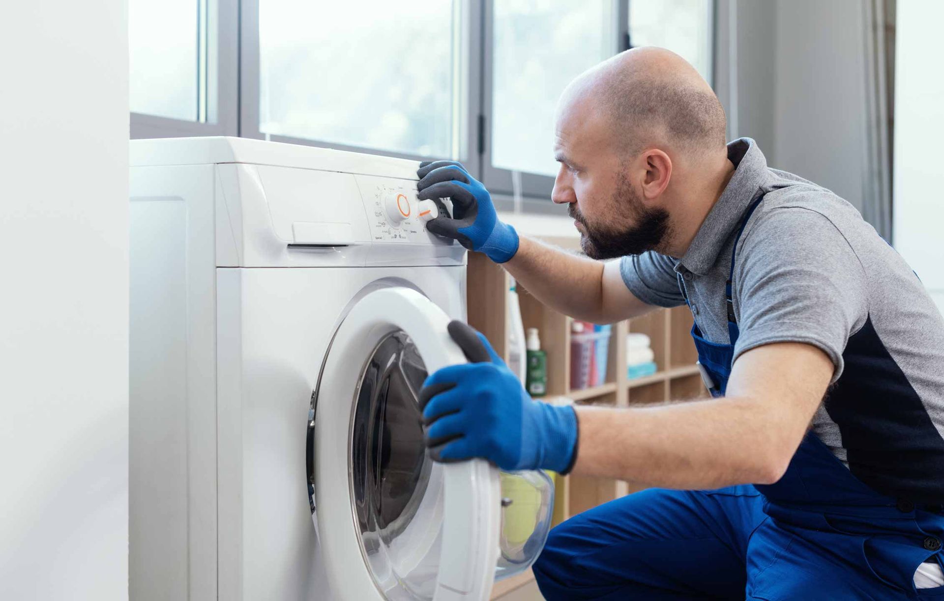 Repair technician fixing a front-loading washing machine in a bright laundry room