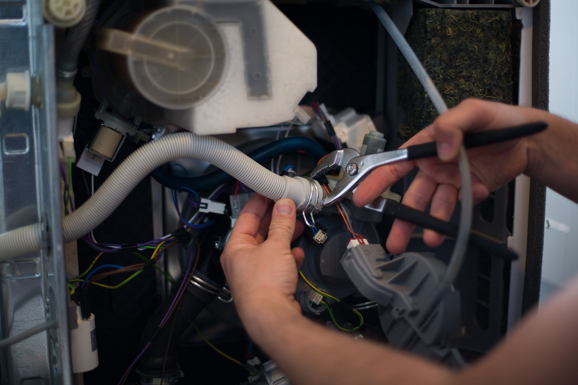 Technician using pliers to repair wiring inside an electronic appliance cabinet