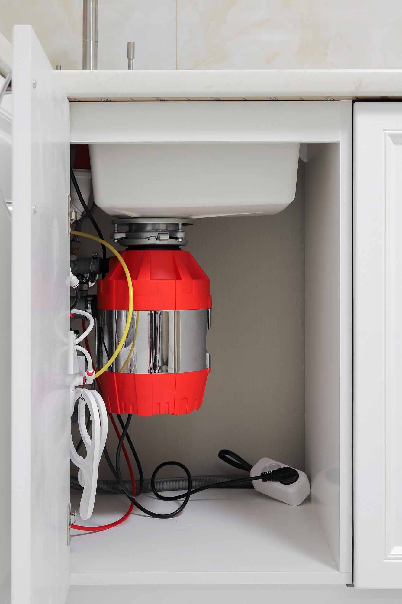 Under-sink cabinet with a red device and white cords plugged in