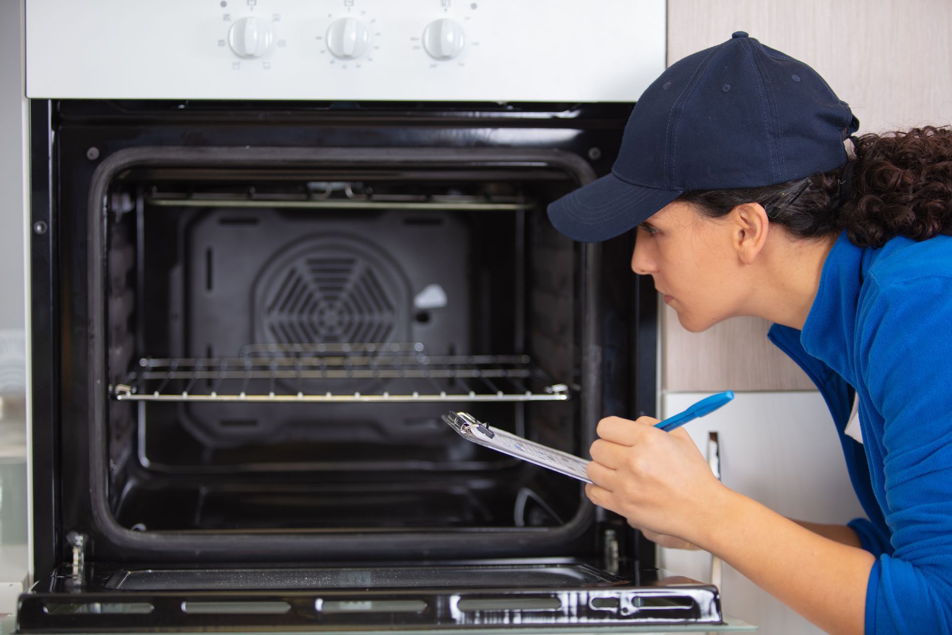 Worker cleaning an oven with a cloth and spray bottle in a kitchen