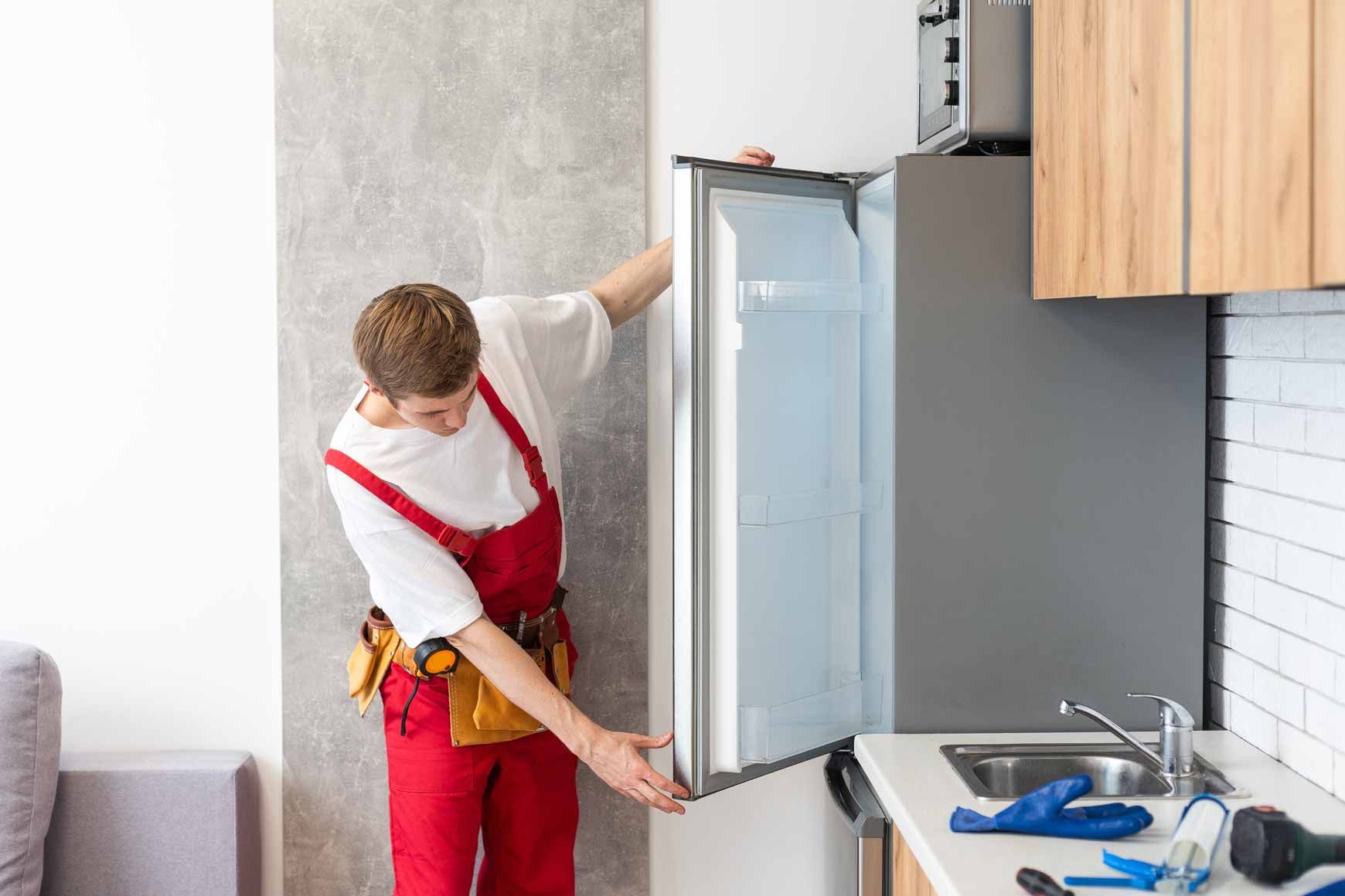 Technician in red overalls opening a refrigerator in a kitchen