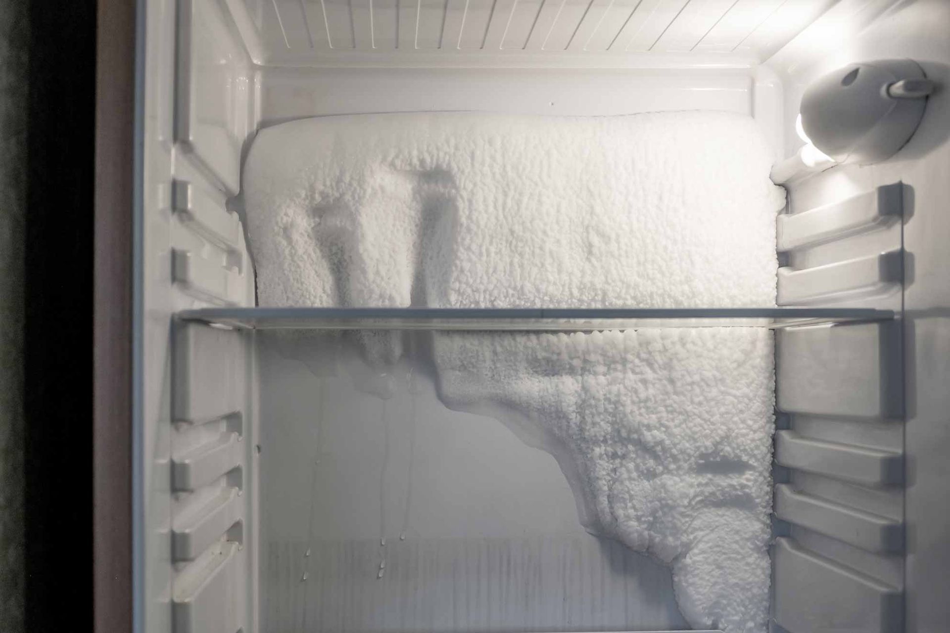 Inside a freezer, thick frost and ice cover the back wall and shelves.