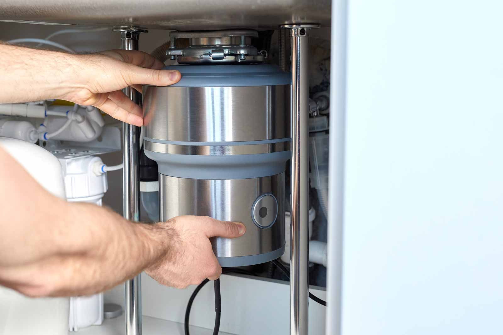 Hands adjusting a metal garbage disposal under a kitchen sink