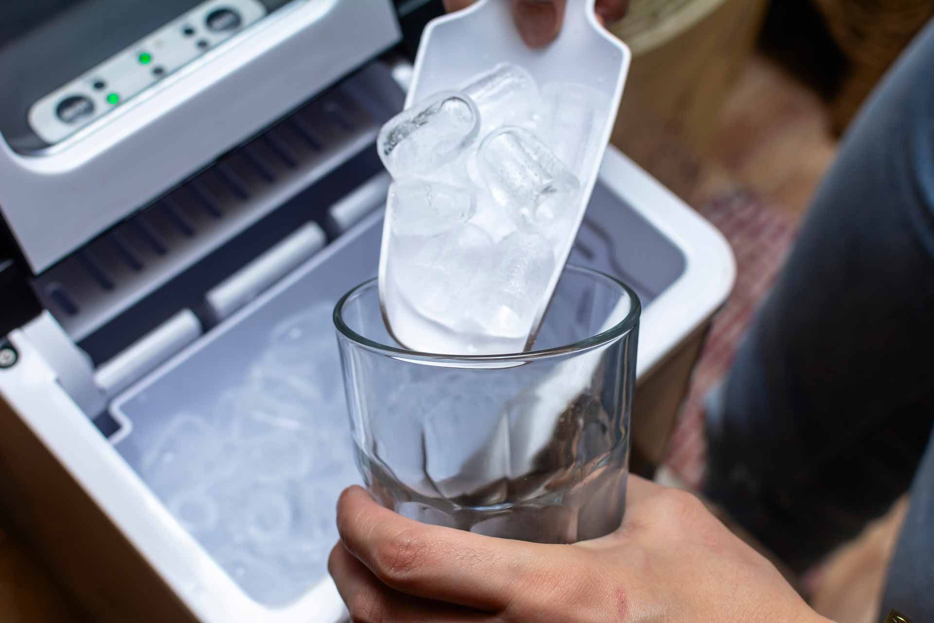Hand placing ice cubes into a clear glass beside an open ice maker