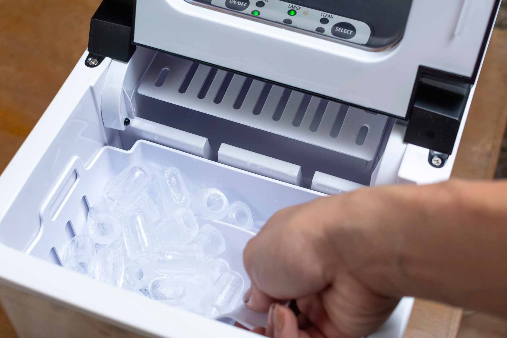 Hand placing clear plastic ice cube tray into a white ice maker drawer
