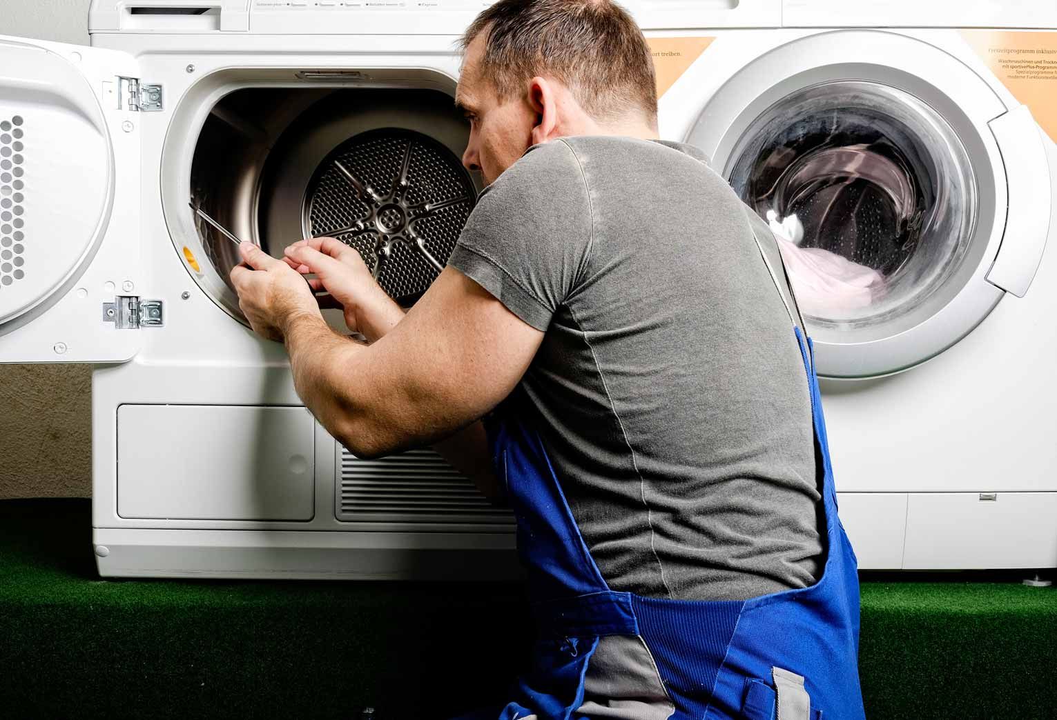Technician repairing a front-loading washing machine in a laundry room