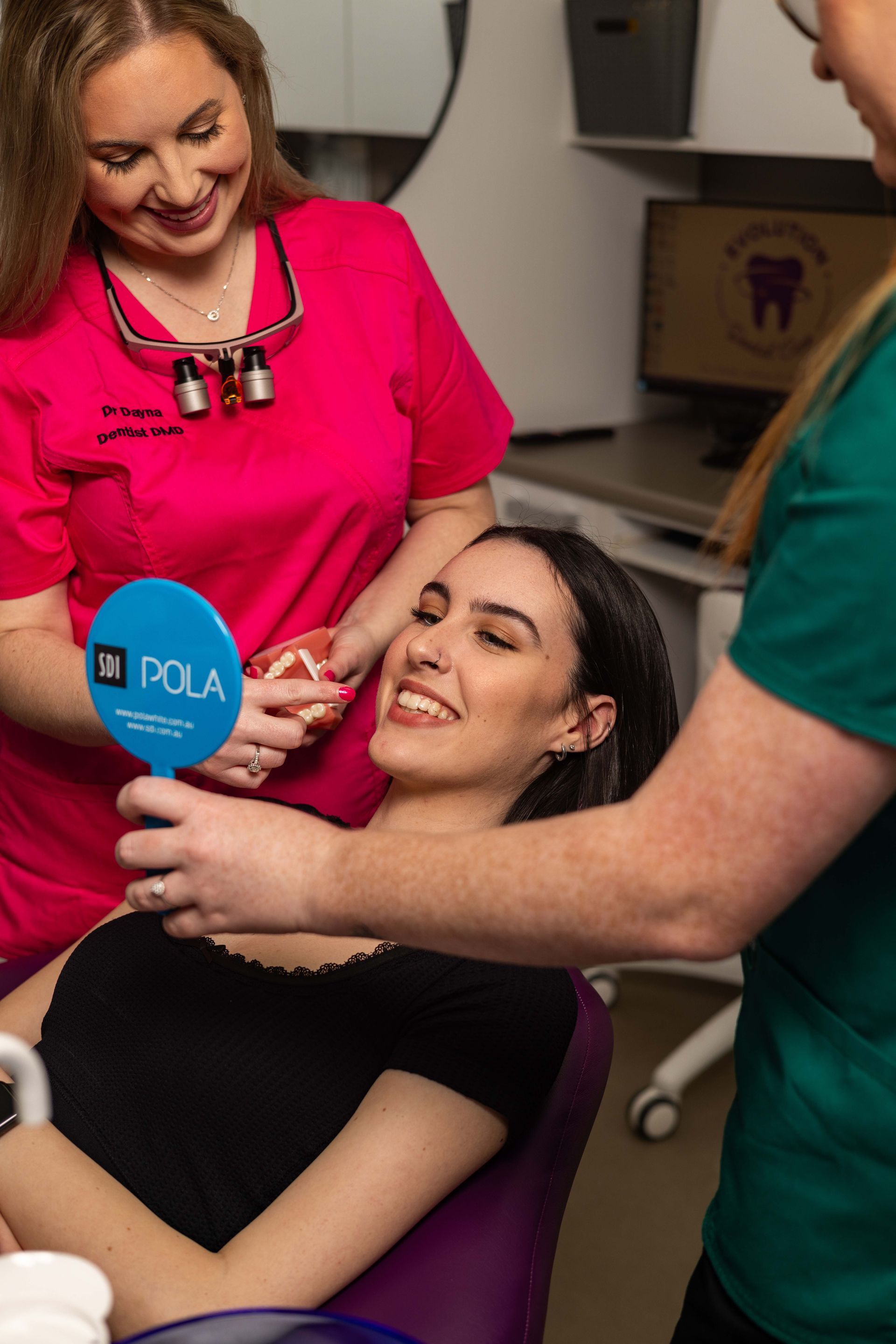 A woman is sitting in a dental chair looking at her teeth in a mirror.