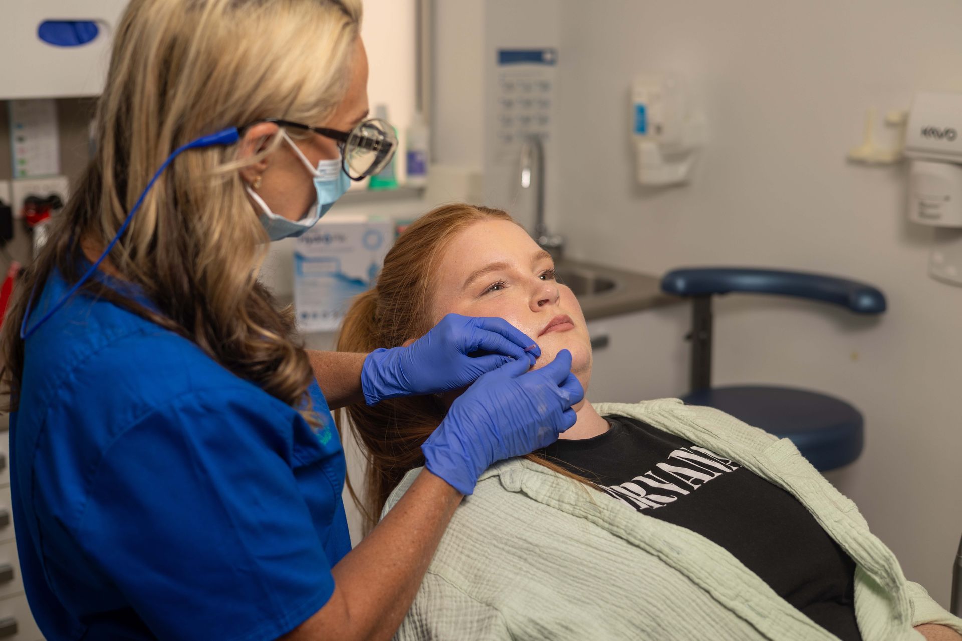 A woman is examining a young girl's face in a dental office.