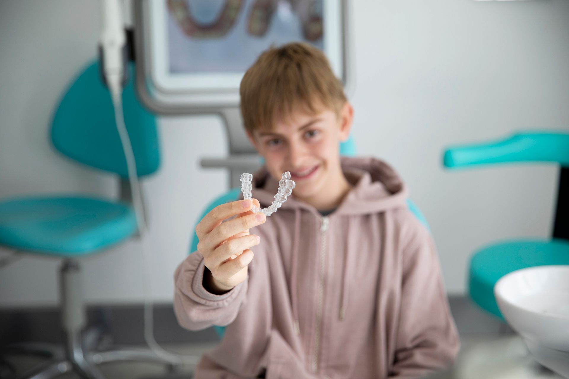A young girl in a blue shirt is holding a dental retainer