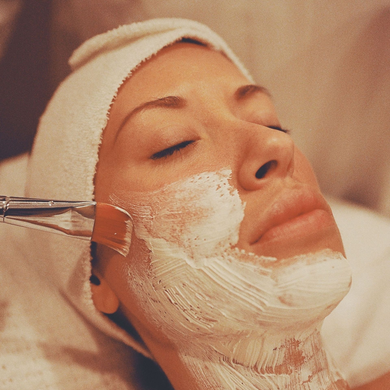 Person receiving a facial cream treatment while lying with eyes closed, covered in white cream on the face