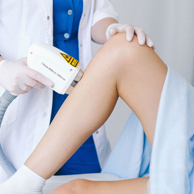 Technician using a laser hair removal device on a leg during a medical treatment