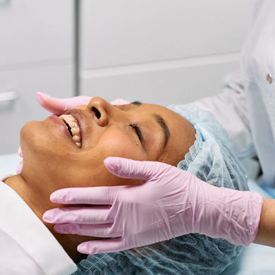 Dentist in pink gloves examining a smiling patient with a hair cover in a clinic