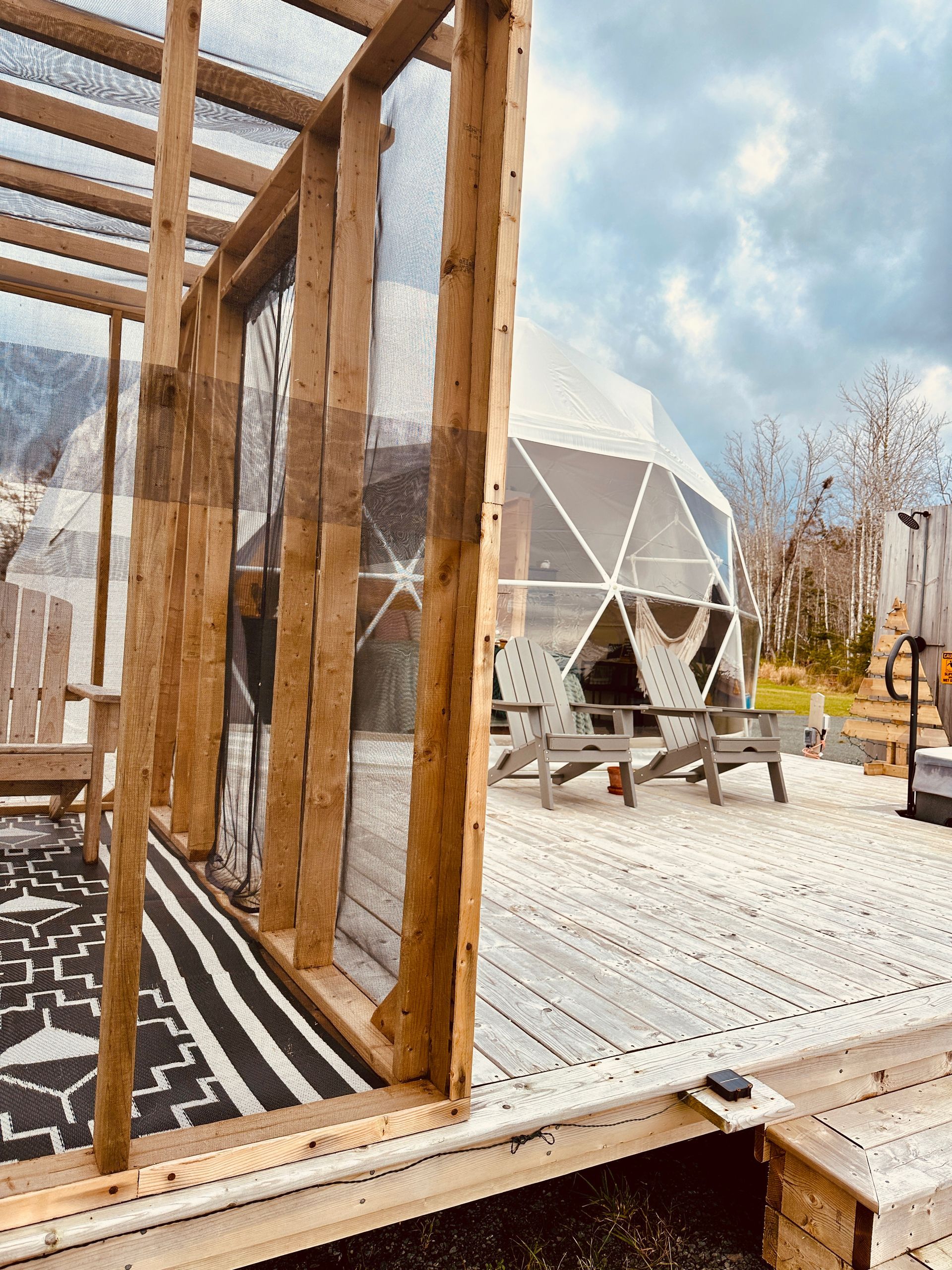 Wooden deck with chairs, view of a dome structure, and a patterned rug. Cloudy sky.