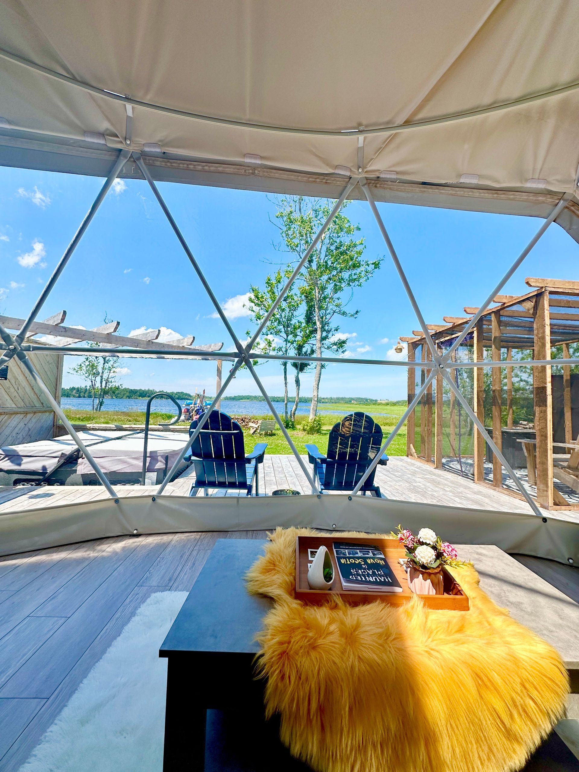 Interior view of a geodesic dome with a table and a view of lake and Adirondack chairs.